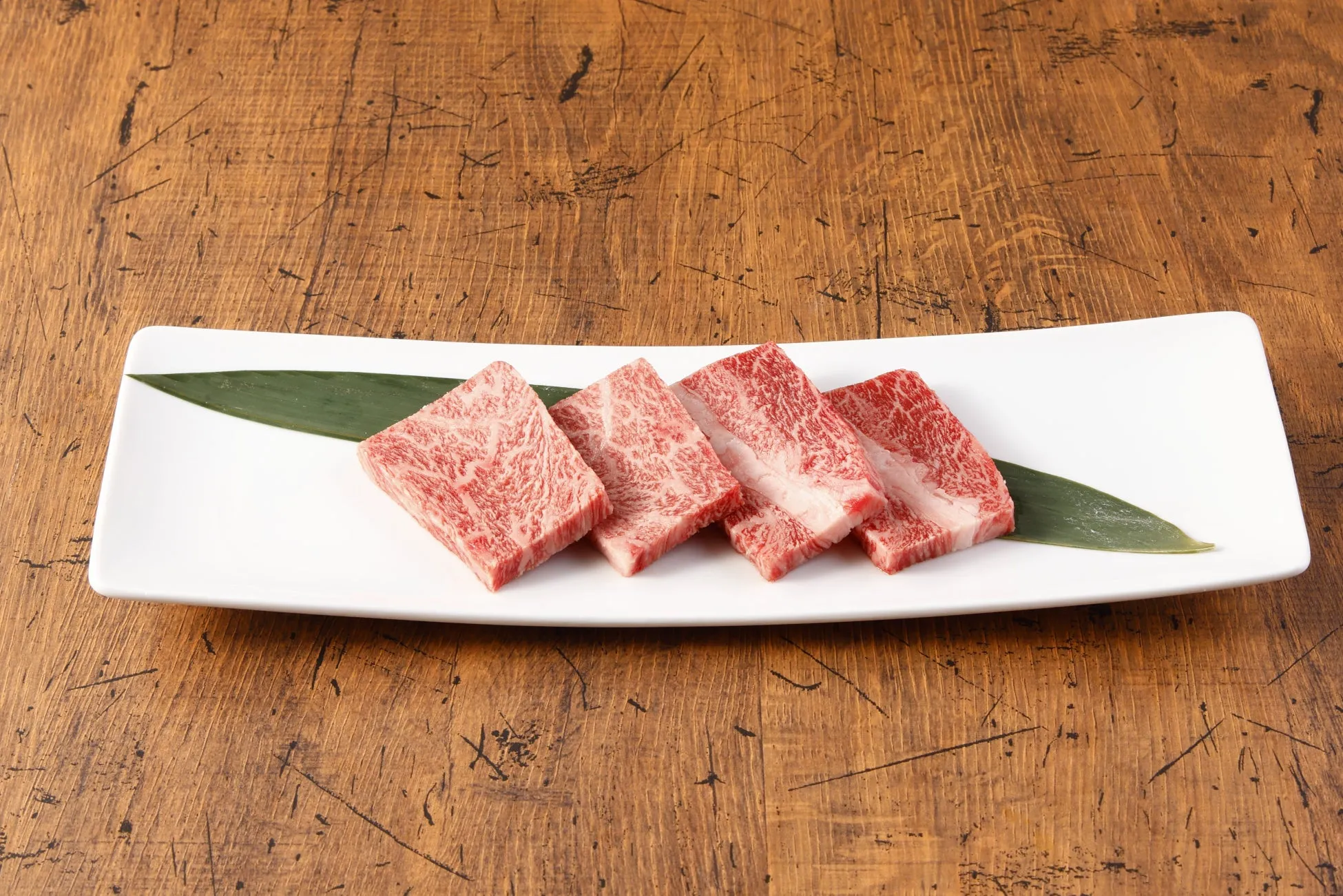 白い皿に盛られた、霜降りの牛肉の美しい写真。葉っぱが添えられており、木製の背景が高級感を演出しています。