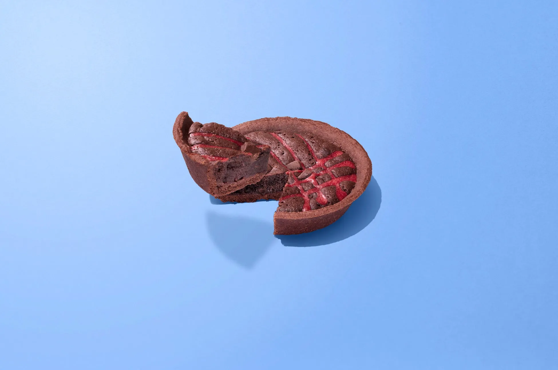 青色の背景に、チョコレートタルトの一部が切り取られた画像です。タルトは茶色で、赤い模様が入っています。切り取られた部分からは、タルトの中身が見えています。