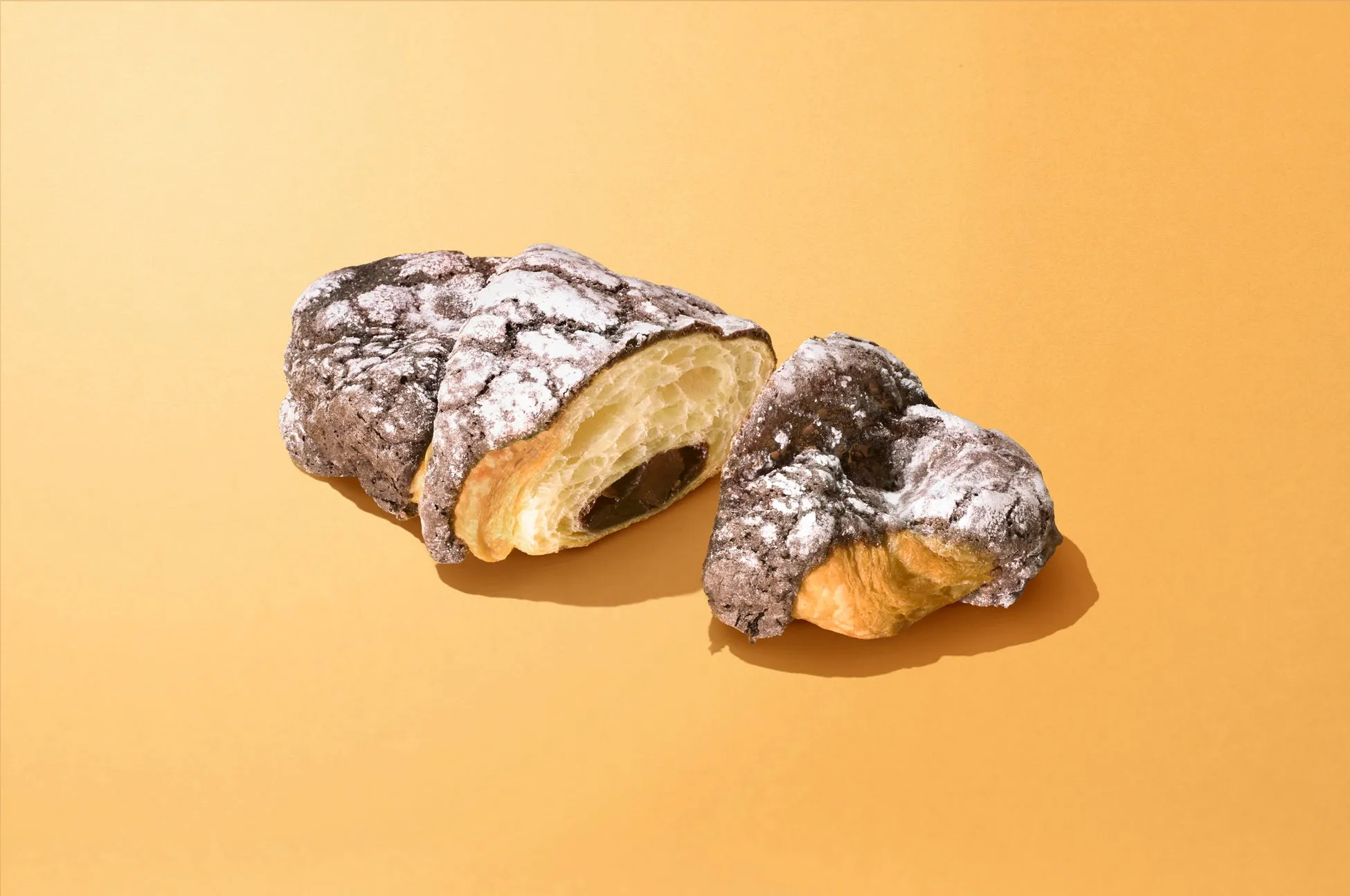 チョコレートクロワッサンが3つ、オレンジ色の背景に置かれています。クロワッサンは半分にカットされており、チョコレートフィリングが見えています。