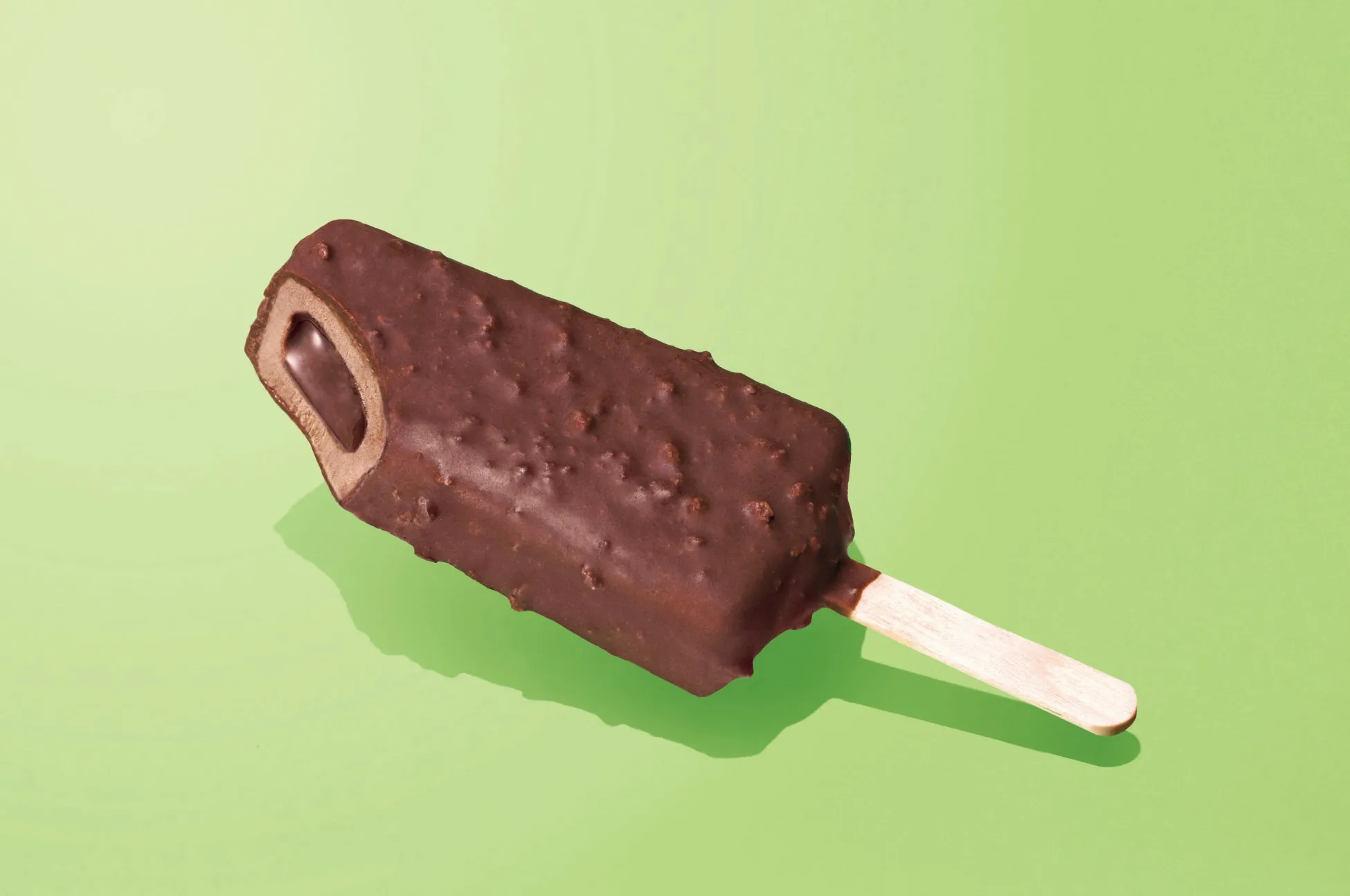 チョコレートでコーティングされたアイスキャンディーが、緑色の背景に置かれています。
