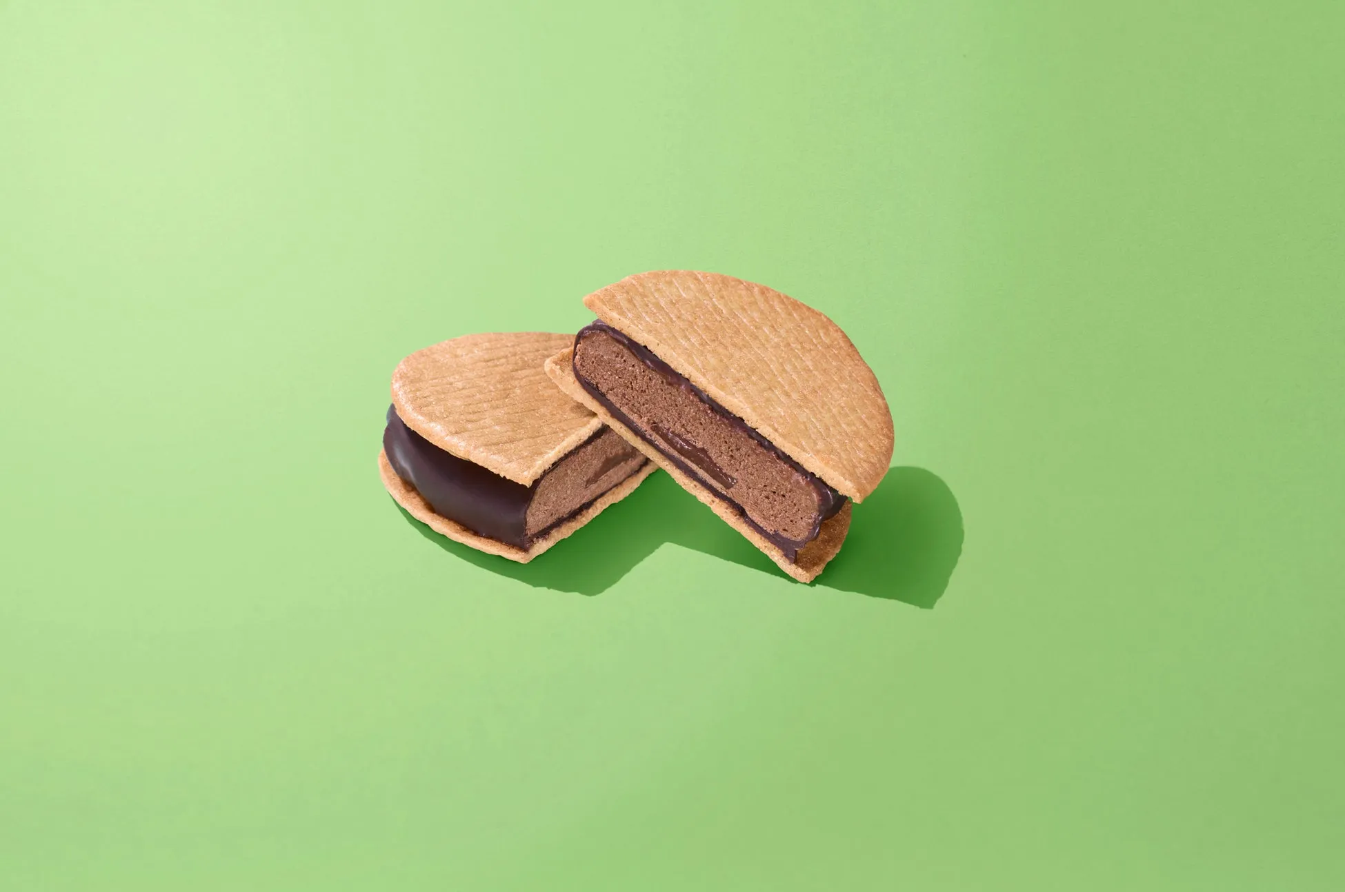 緑色の背景に、チョコレートサンドクッキーが2つ並んでいる写真です。クッキーは半分に割られており、チョコレートフィリングがはっきりと見えます。