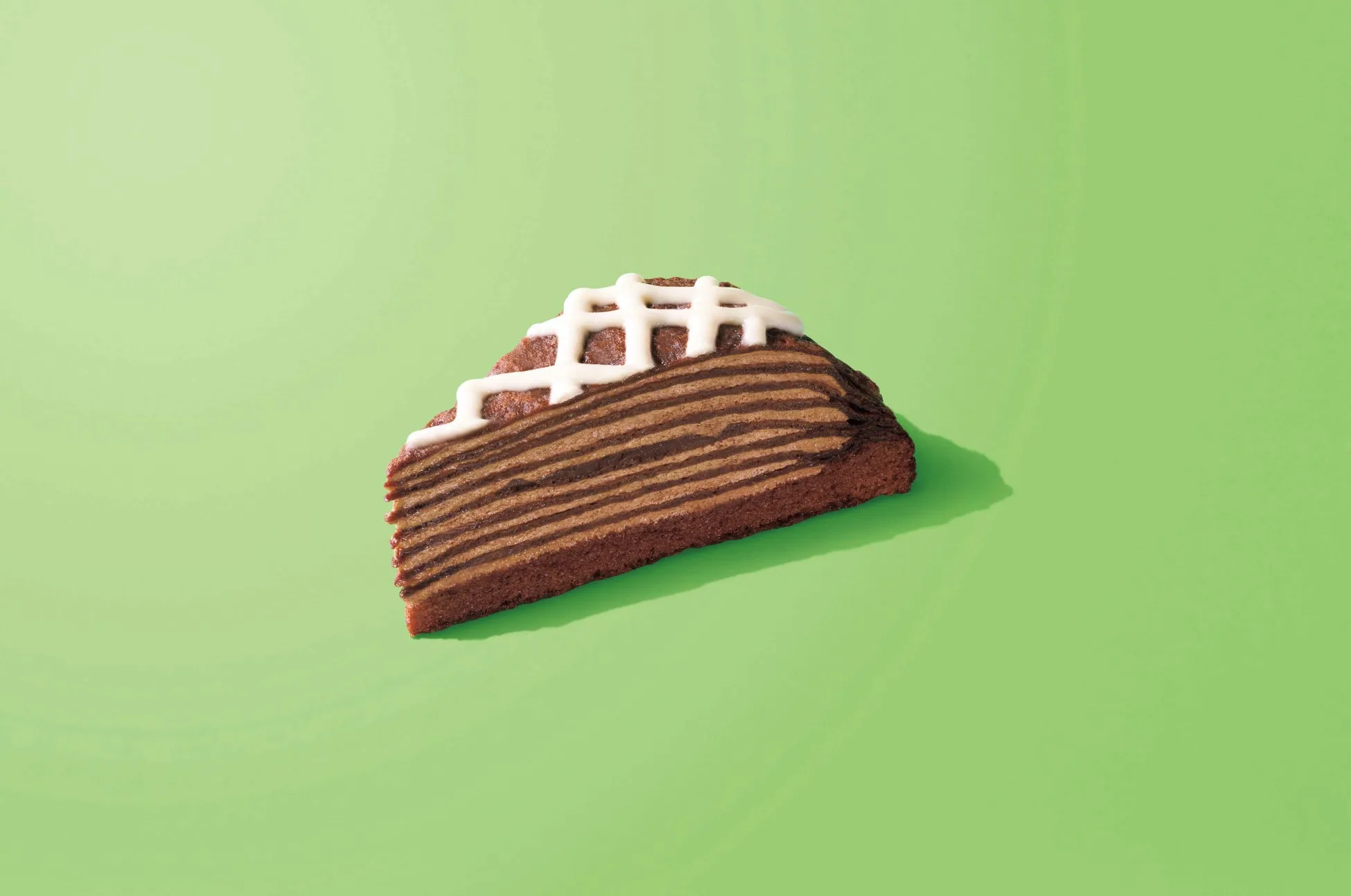 緑色の背景に、チョコレートケーキの切り身が一つ置かれています。ケーキの上には白い模様が施されています。