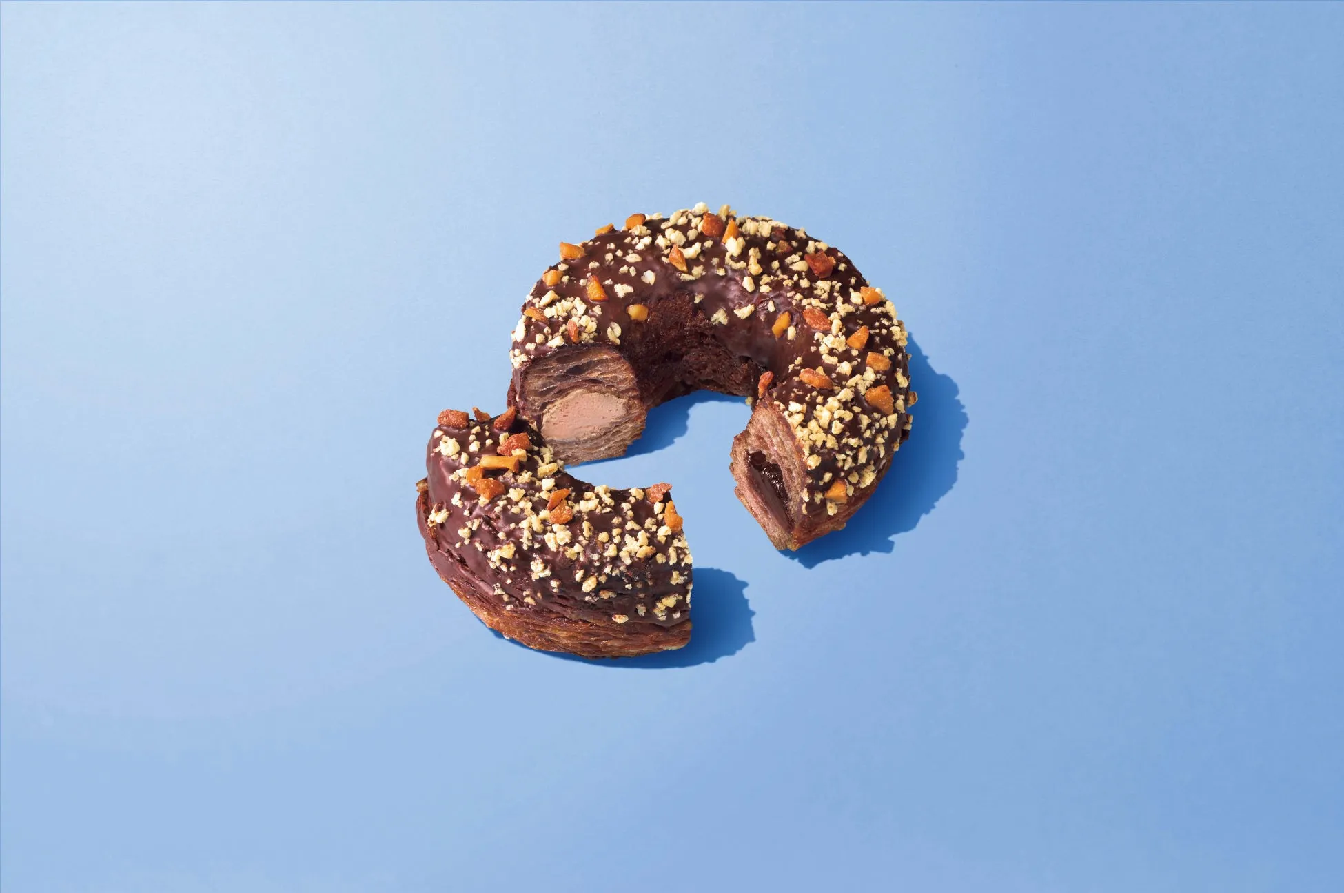 チョコレートでコーティングされ、ナッツがトッピングされたドーナツ。一部が切り取られ、内部の層が見えています。背景は青色です。