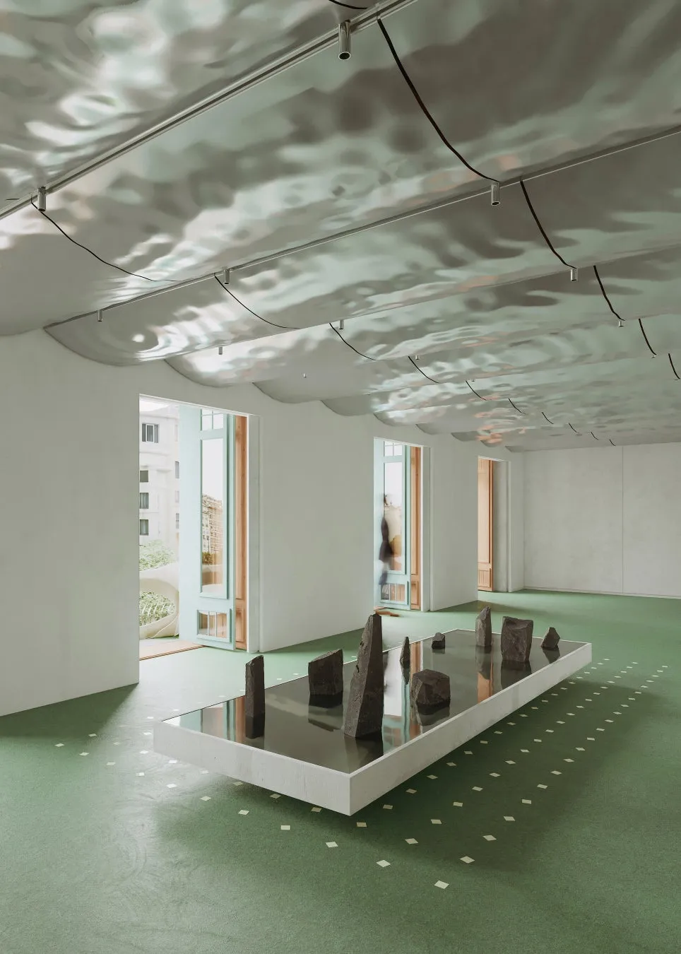 水面を模した天井と、中央に石が置かれた池のようなオブジェがある空間の写真