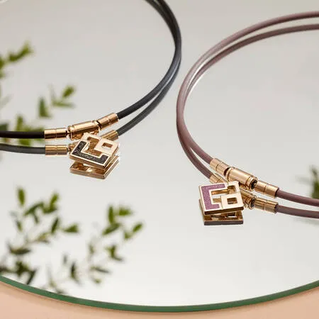 2つのネックレスが映った写真。ネックレスは、黒と茶色のコードと、金色の装飾とロゴが付いた正方形のペンダントで構成されている。