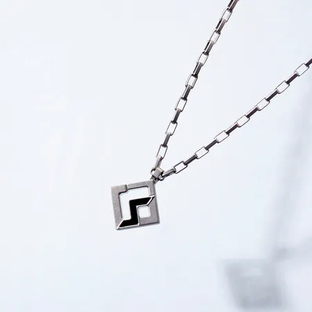 白い背景に、正方形のペンダントトップが付いたシルバーのネックレスが写っています。ペンダントトップには黒い模様が入っています。