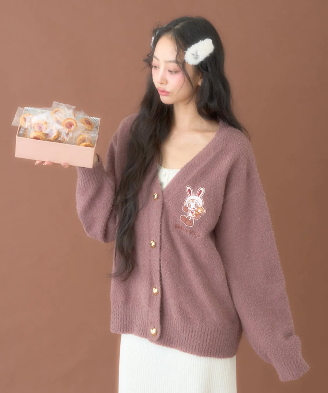 女性がピンク色のカーディガンを着て、お菓子が入った箱を持っている写真