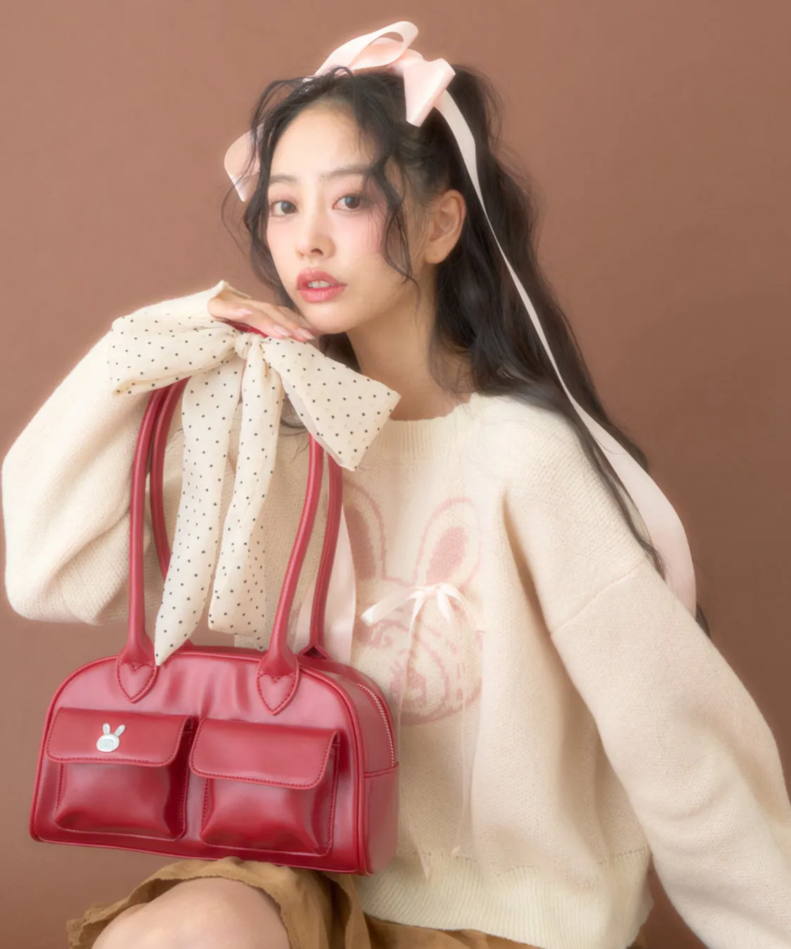 女性が赤いバッグを持ち、ピンクのリボンとウサギの絵柄のセーターを着ている写真