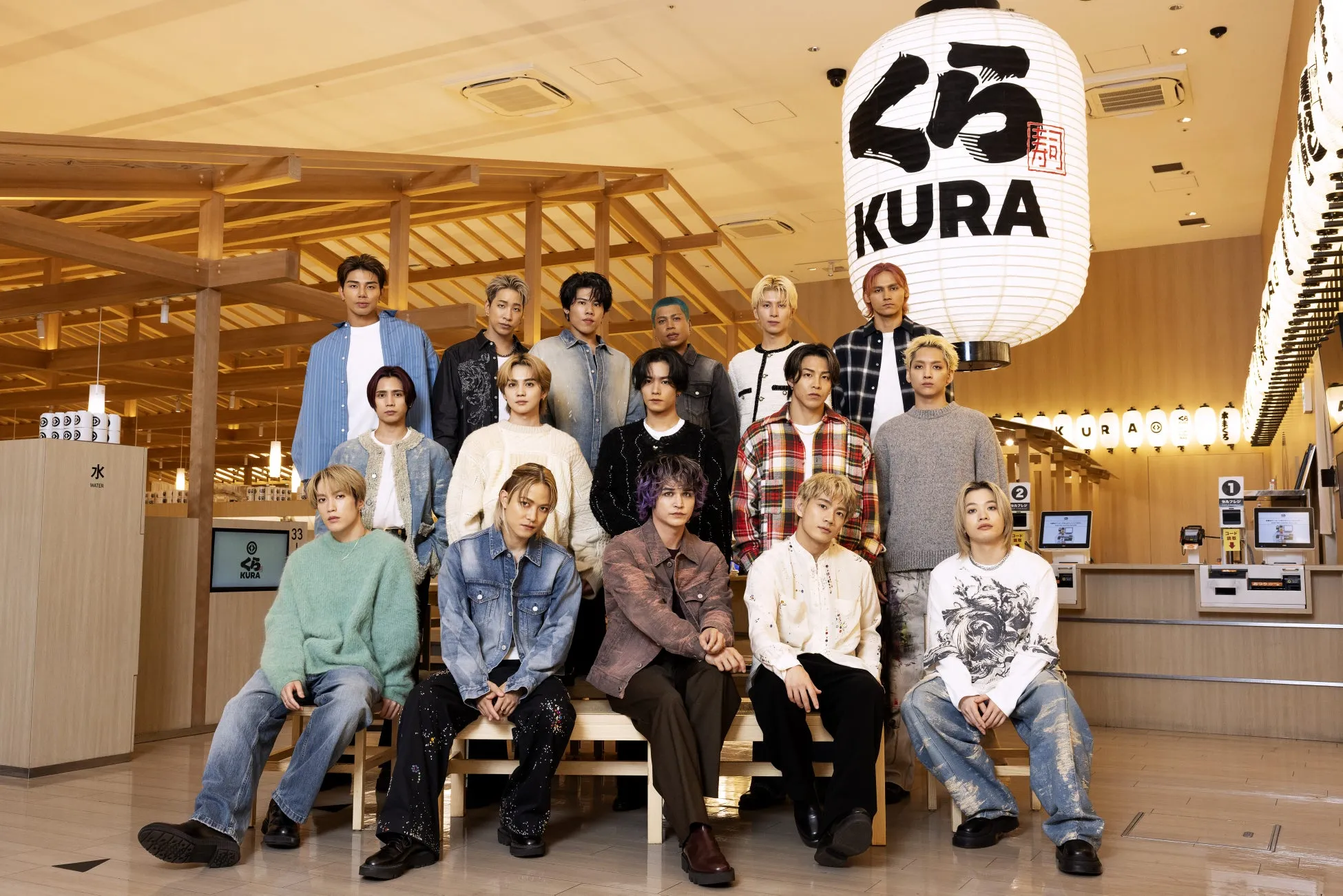 KURAの店内で、15人の男性グループがポーズをとっている写真。大きな提灯には「くら」の文字が書かれており、グループはカジュアルな服装をしている。