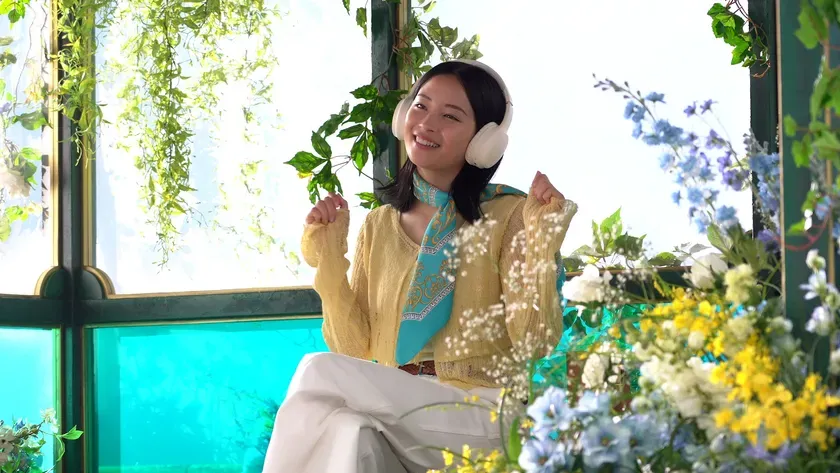 女性がイヤホンをして花に囲まれて座っている様子