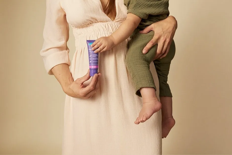 女性が子供を抱きかかえ、紫色のチューブに入った製品を持っている様子。