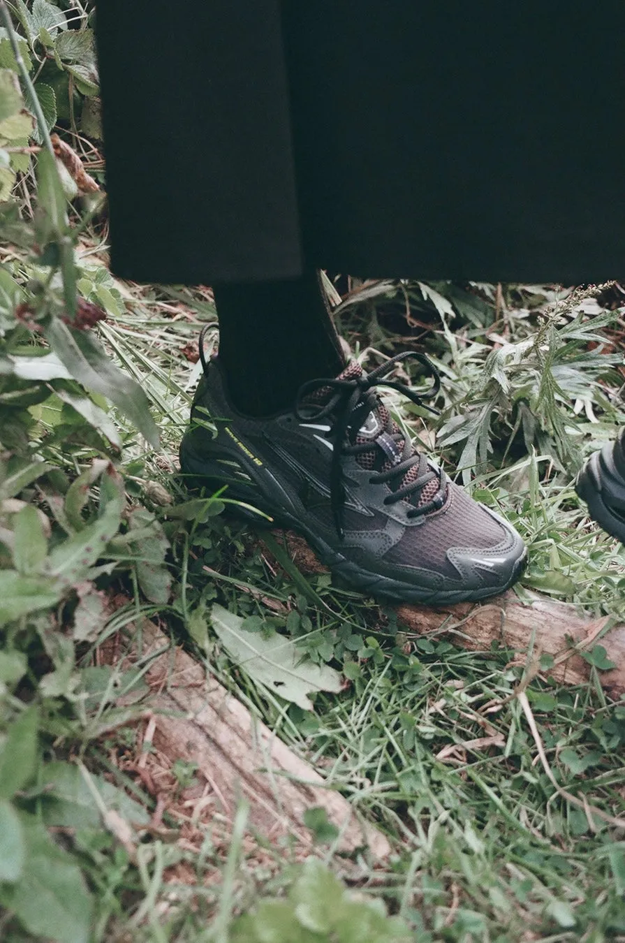 黒いスニーカーを履いた足元が、草の上に置かれた丸太の上に立っている。