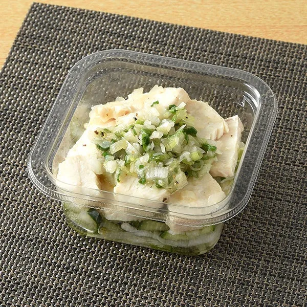 透明な容器に入った鶏肉料理。鶏肉は一口大にカットされ、ネギや香味野菜のソースがかけられている。容器の底には野菜が敷き詰められている。