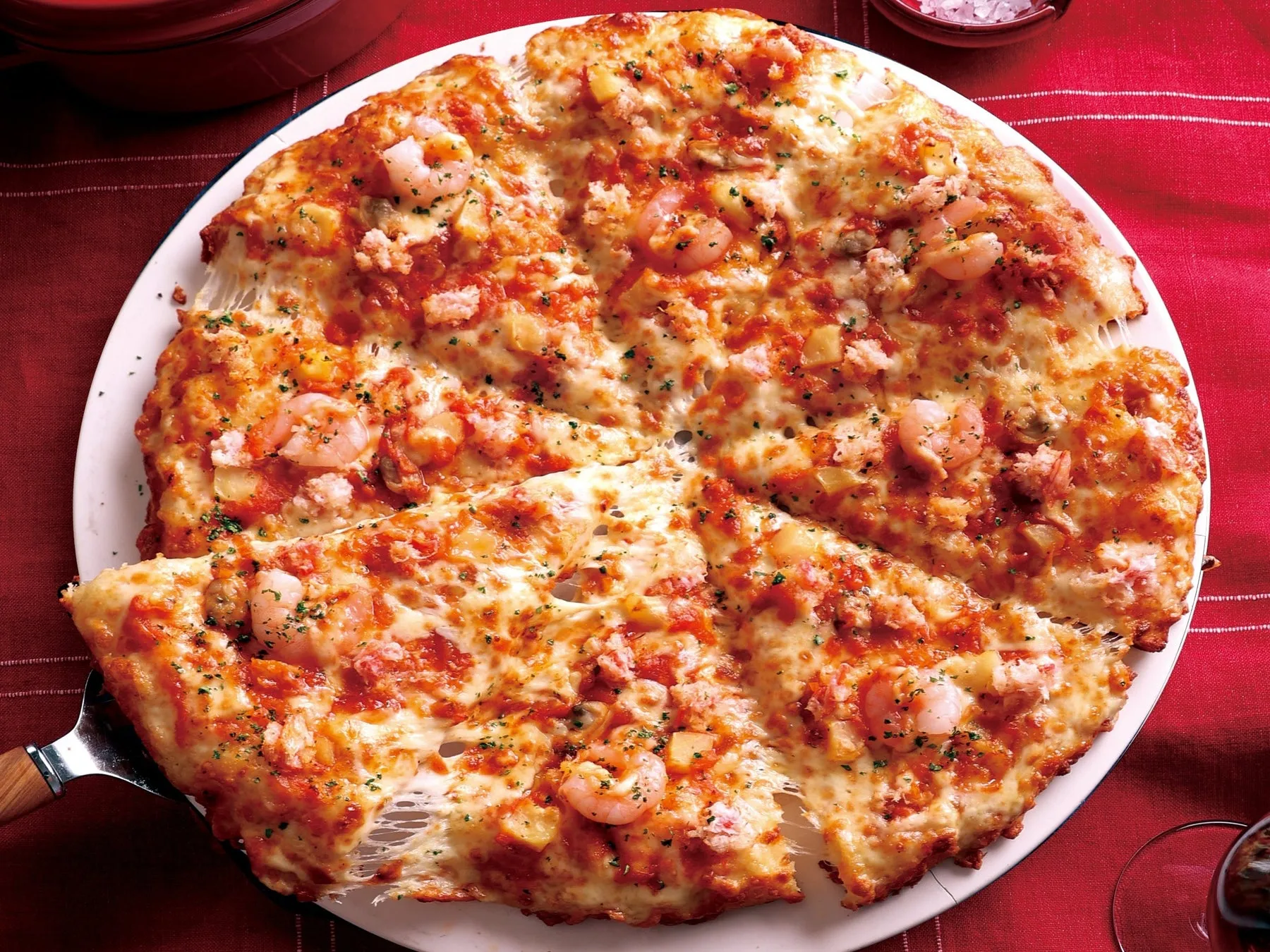 エビとチーズがたっぷり乗ったピザの画像です。ピザはカットされており、一切れが持ち上げられています。
