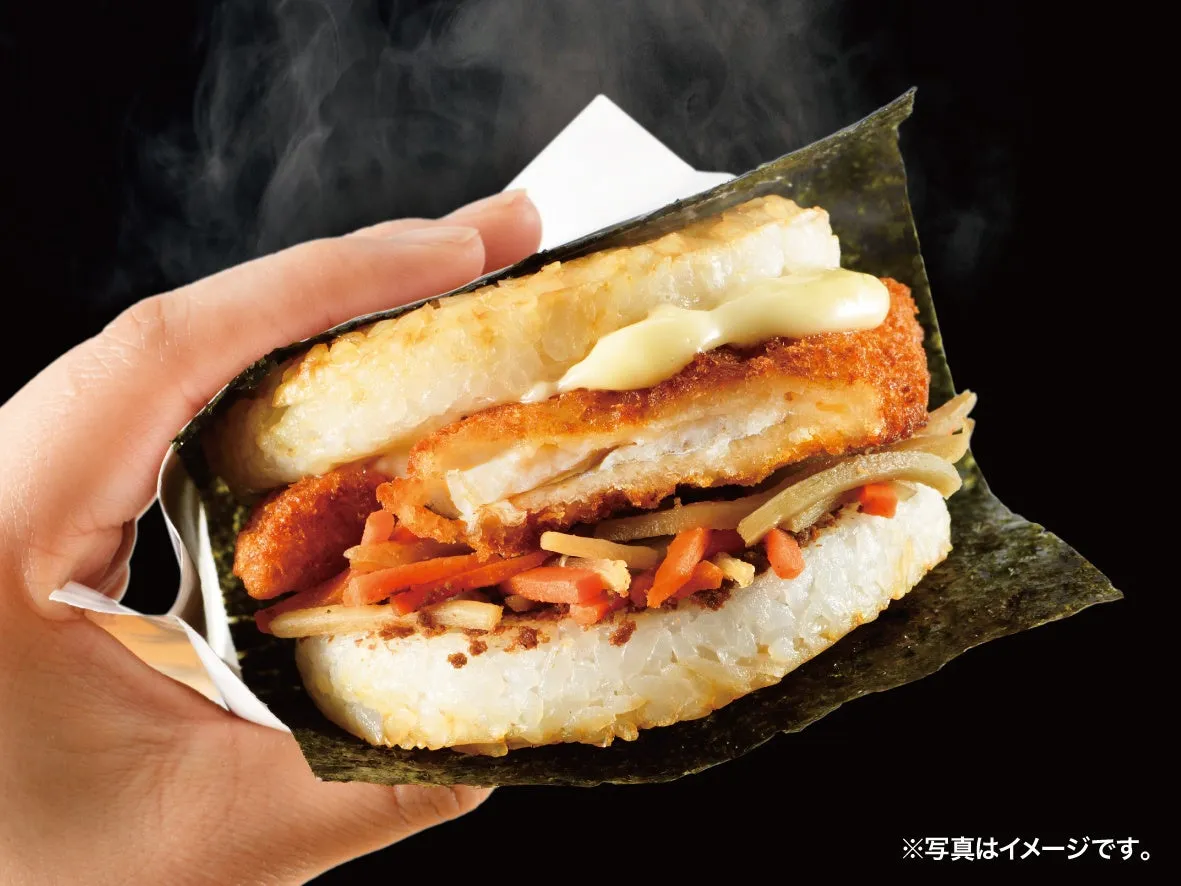 海苔で包まれたご飯で、揚げ物や野菜を挟んだ食べ物。手で持たれており、湯気が立っている。