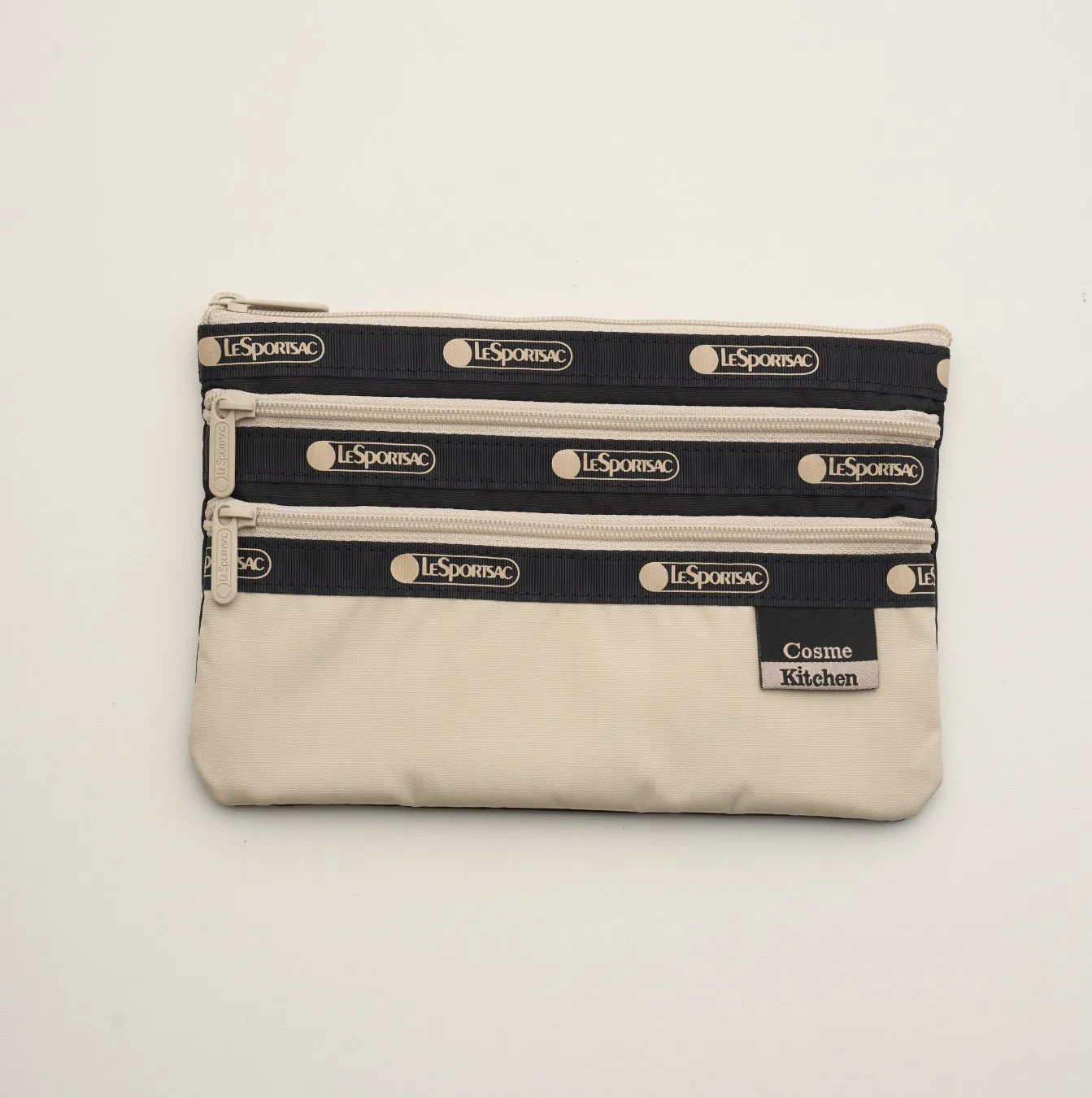 LeSportsacのコスメポーチ。黒とベージュの配色で、前面に3つのファスナーが付いています。ブランドロゴが繰り返し配置されています。