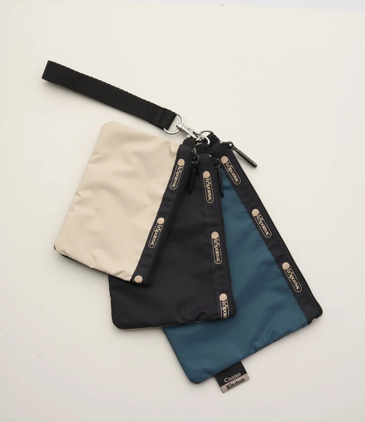 3つのポーチが重なって配置された画像です。一番手前にある青いポーチには「Cosme Kitchen」のタグが付いています。他の2つのポーチは、黒とベージュで、それぞれ「LeSportsac」のロゴが入ったジッパーが付いています。ポーチは、黒いストラップとシルバーの金具で繋がっています。