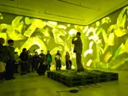 舞台でパフォーマンスをしている人々と、それを見ている観客の様子を捉えた写真です。