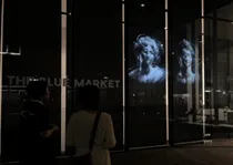 窓ガラスに人物の映像が映し出されており、それを見ている2人の人物が写っている写真です。