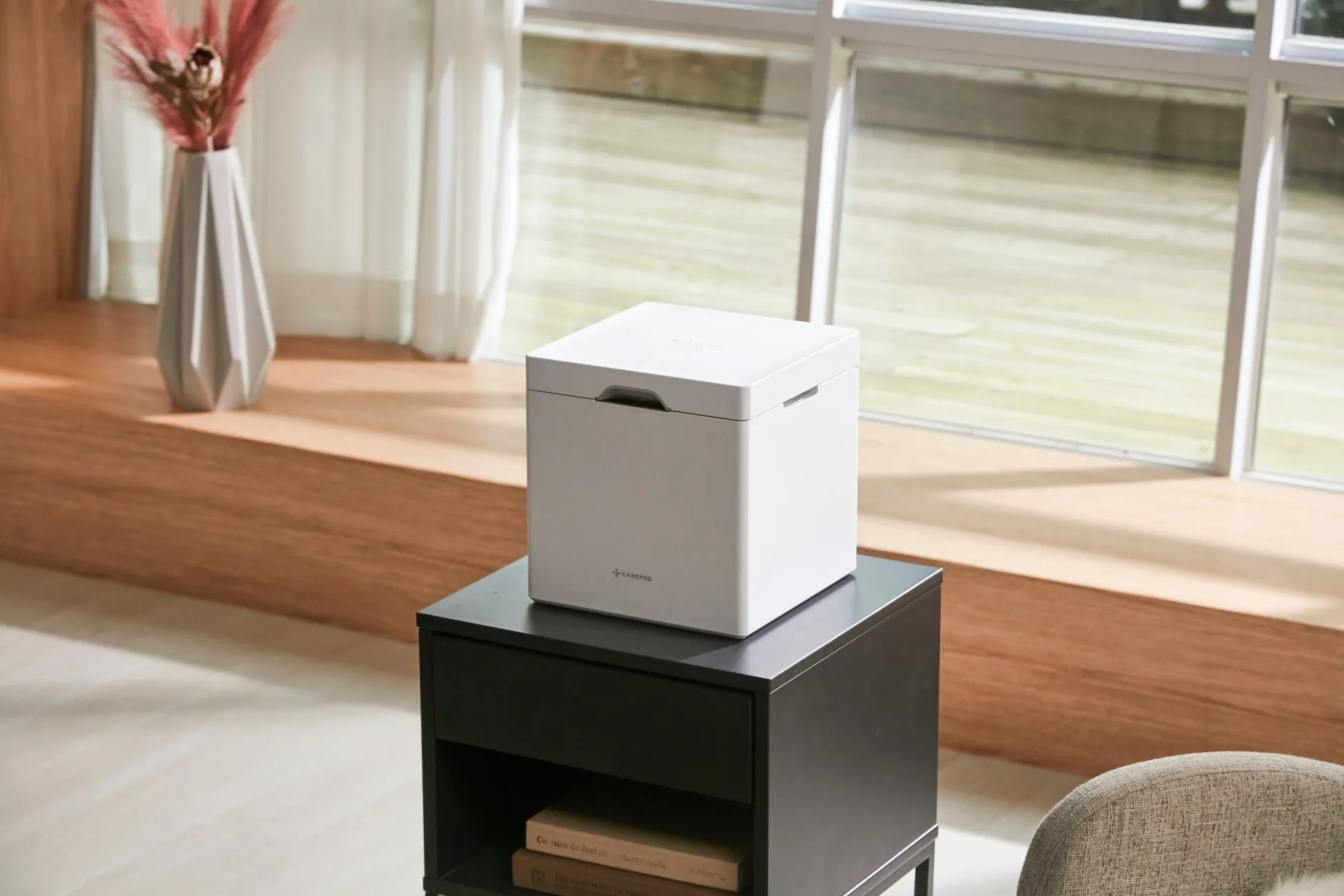 白い箱が黒いサイドテーブルの上に置かれ、窓の近くに花瓶が置かれている写真