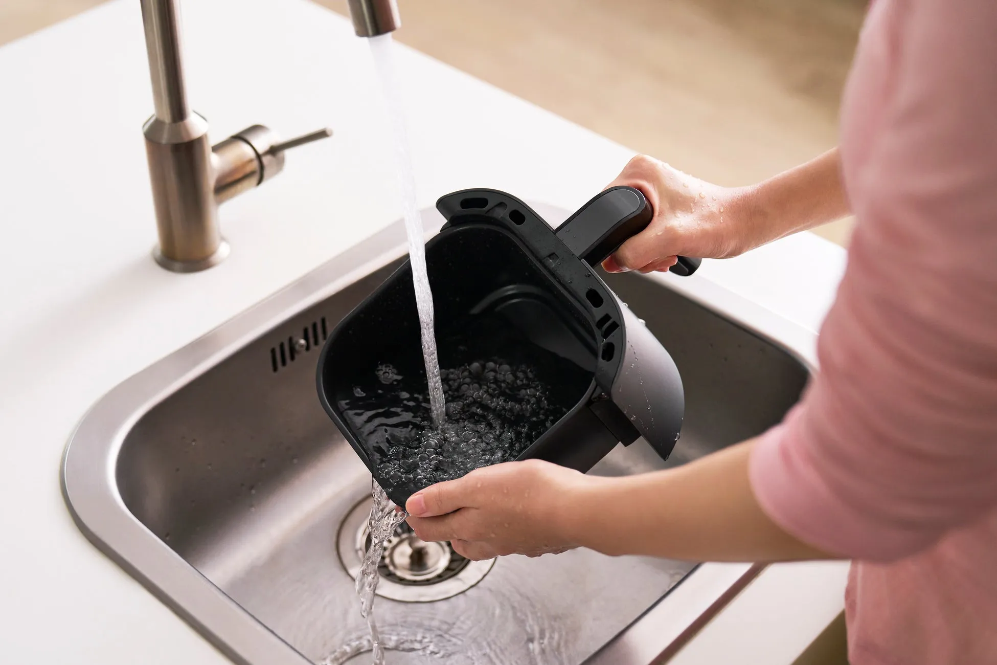 シンクでエアフライヤーのバスケットを洗っている人のクローズアップ。