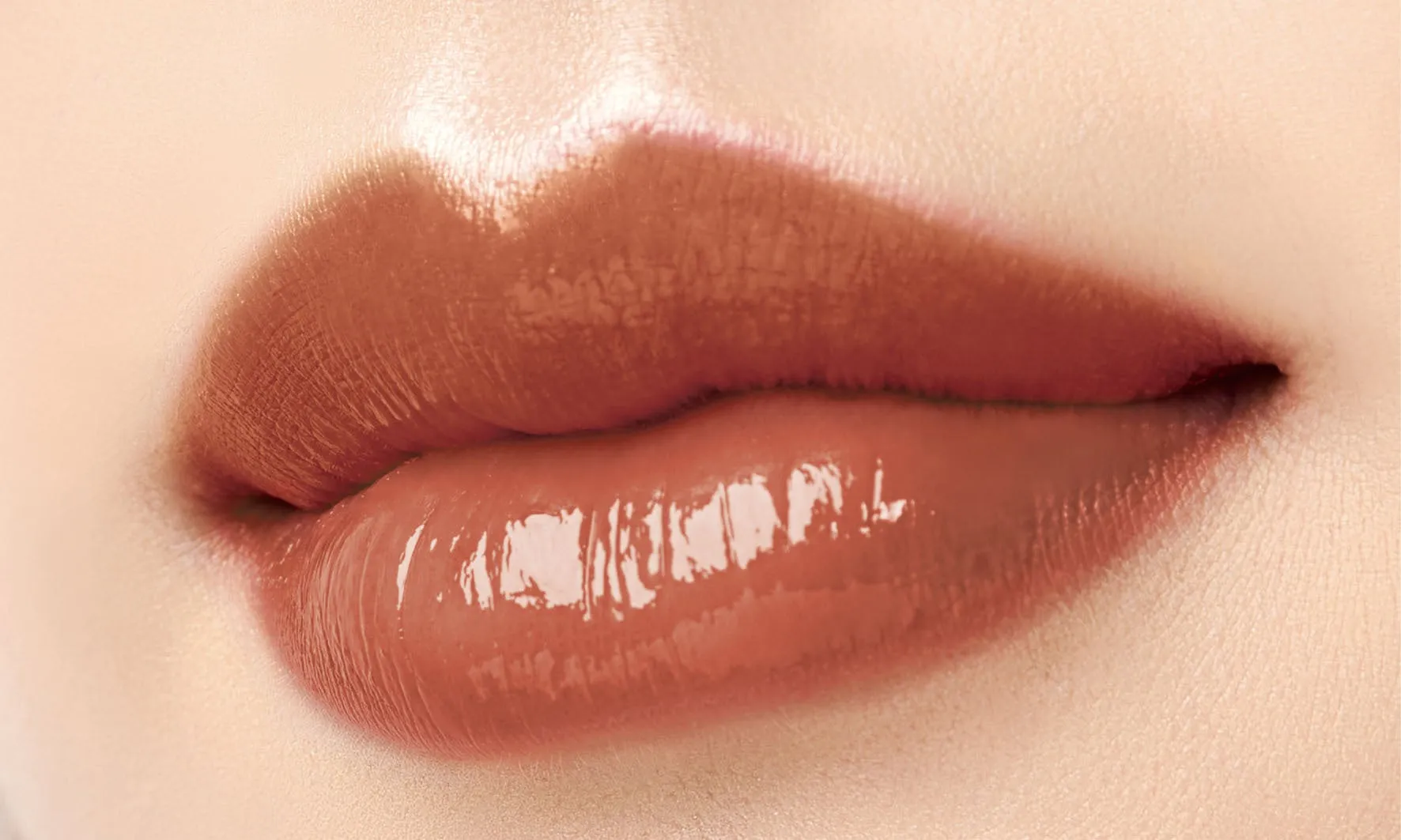 女性の唇のクローズアップ。唇は光沢のある茶色で、肌は明るい。