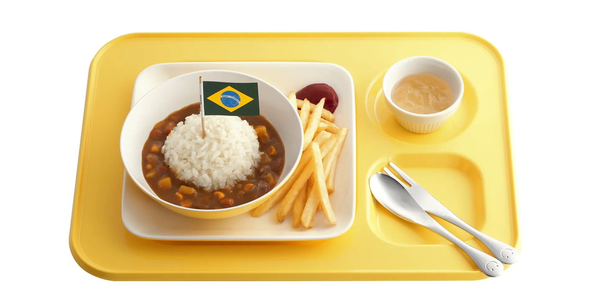 黄色いランチトレイの上に、カレーとご飯、フライドポテト、ソース、デザート、ブラジルの国旗が乗った食べ物