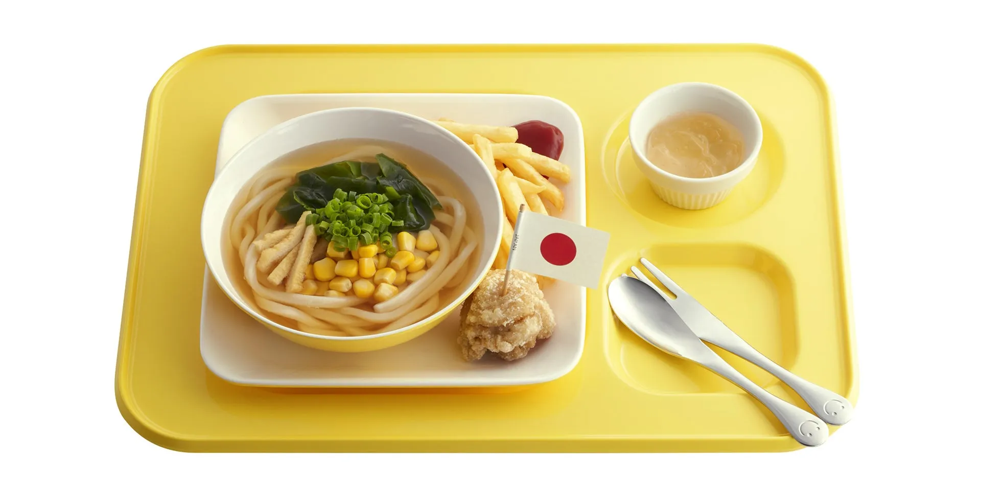 黄色いランチトレイに、うどん、フライドポテト、ソース、揚げ物、日本国旗、フォークとスプーンが置かれた日本の学校給食の画像
