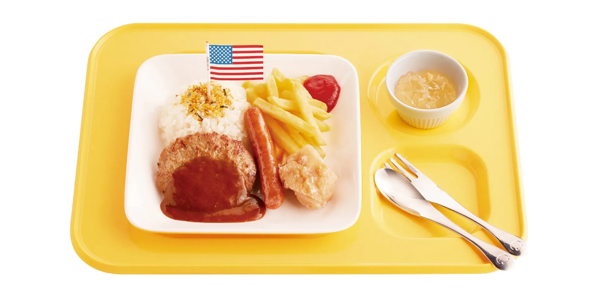 黄色いランチトレイに、ハンバーグ、ご飯、フライドポテト、ソーセージ、鶏の唐揚げ、ゼリー、アメリカ国旗が添えられた給食のような料理