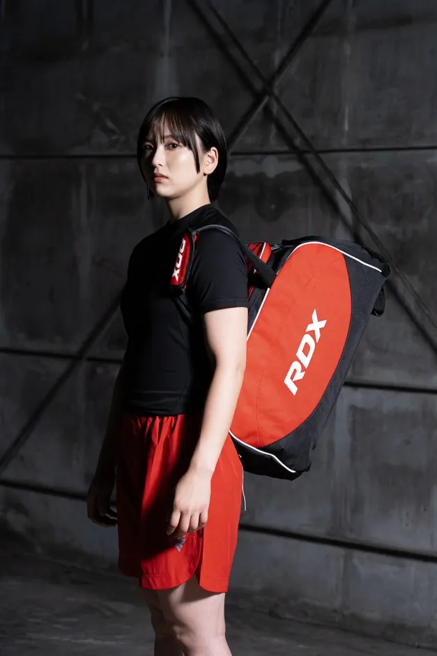 黒いTシャツと赤いショートパンツを着た女性が、RDXと書かれた赤いバッグを肩にかけている写真