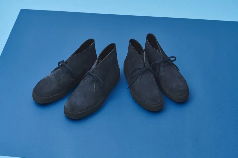 青い背景に置かれた、紺色のスエードのチャッカブーツのペアのクローズアップ画像。