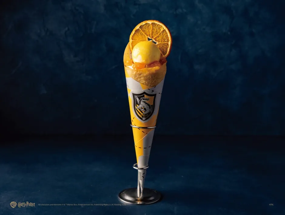 ハリーポッターをテーマにした、黄色とグレーの円錐形の容器に入ったデザート。デザートはオレンジのスライスとアイスクリームで飾られています。