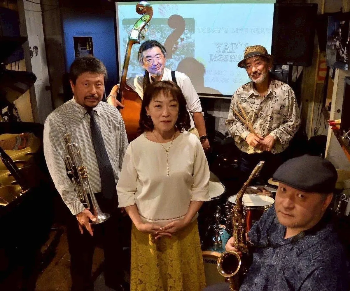 ジャズバンドの集合写真。女性を含む5人のメンバーが写っており、楽器を持ったり、演奏の準備をしている様子が写っている。