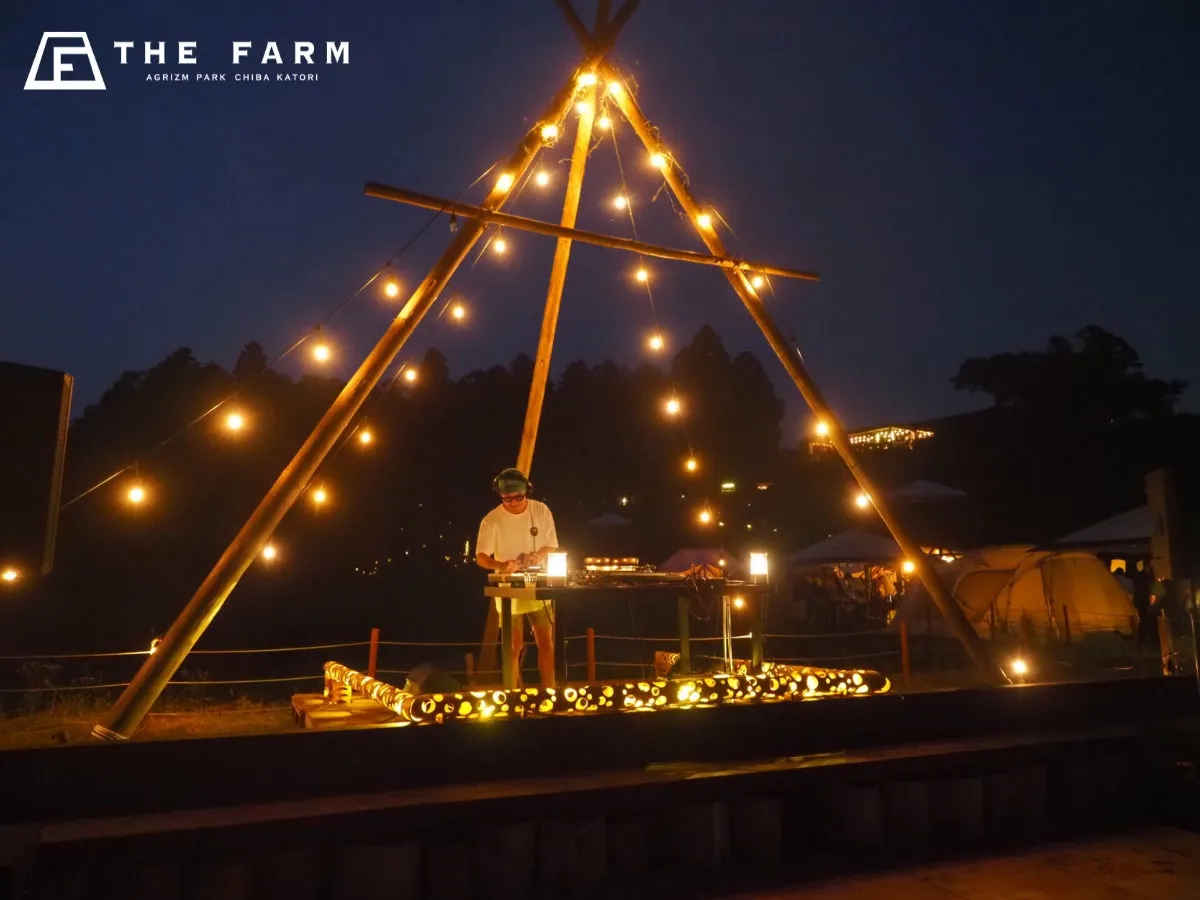 夜の野外イベントの様子。DJが音楽を流し、照明が飾られたステージで盛り上がっている。