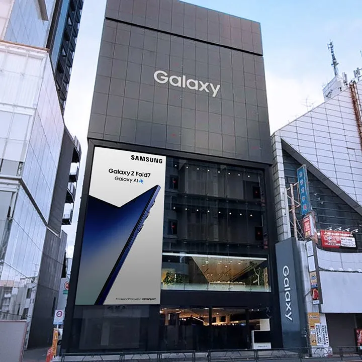 サムスンのGalaxyブランドの店舗の正面玄関の画像です。看板には、Galaxy Z Fold7とGalaxy AIが宣伝されています。建物の外観はモダンで、ガラス張りの窓と、Galaxyのロゴが大きく表示されています。