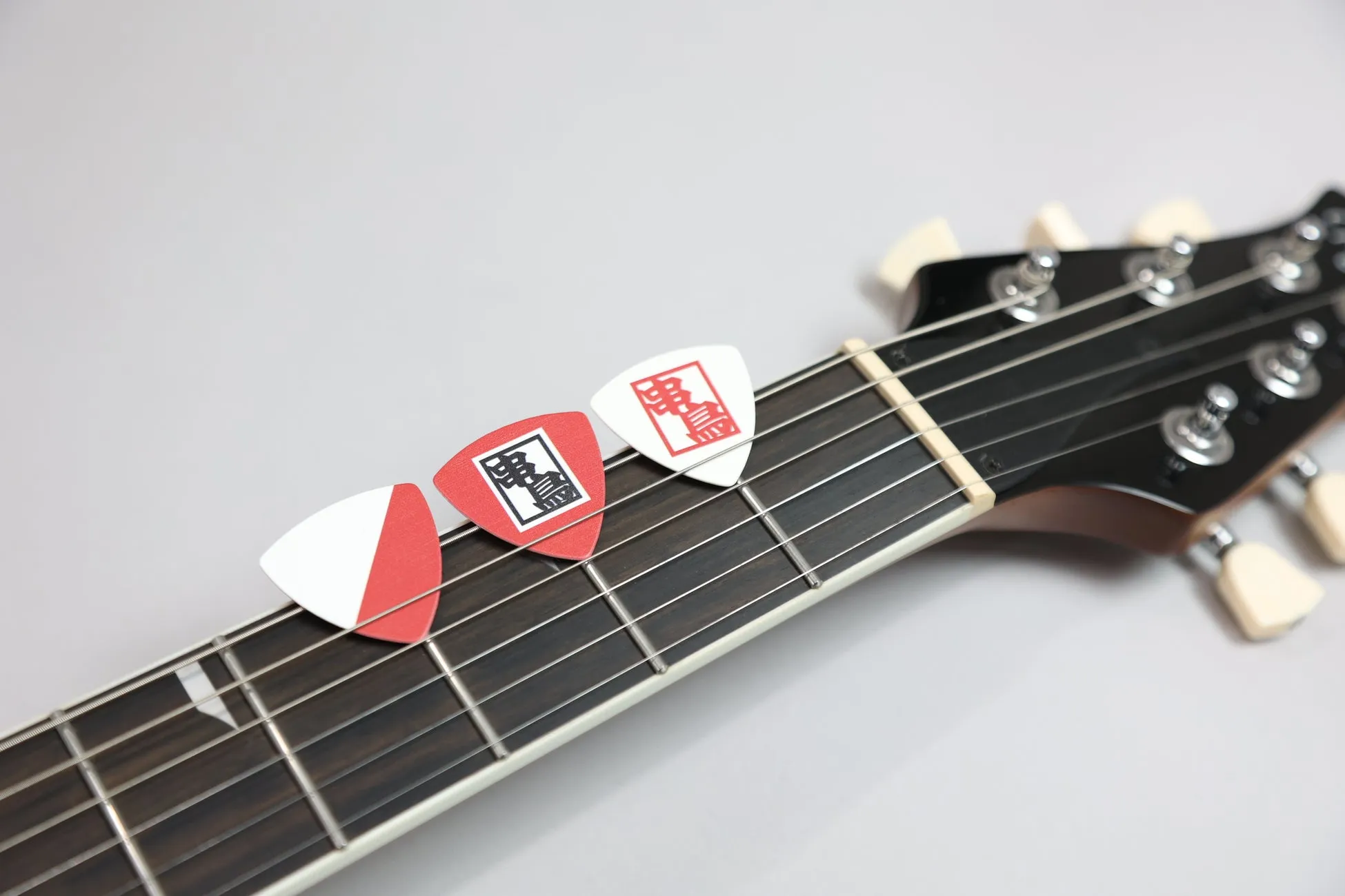 ギターのヘッドストックとピックが写っている写真。ピックには「明言」という文字が書かれている。