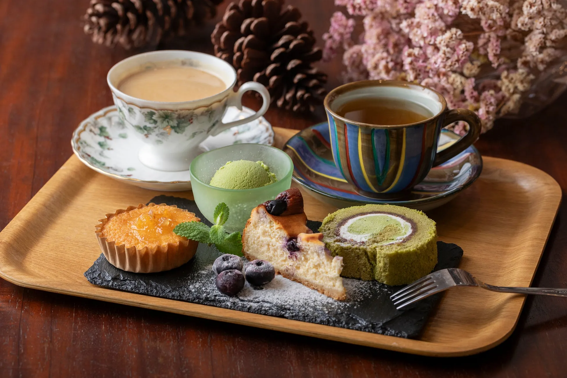 木製のトレーに、ケーキ、抹茶アイス、紅茶、コーヒーが乗ったおしゃれなカフェの風景です。