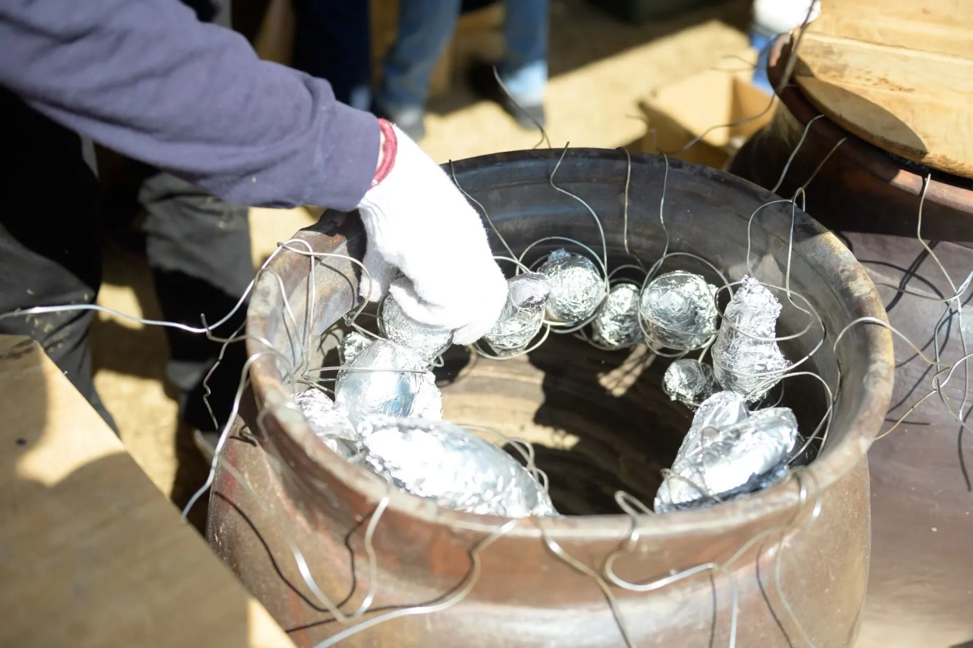 アルミホイルに包まれた食材を大きな壺から取り出している様子。