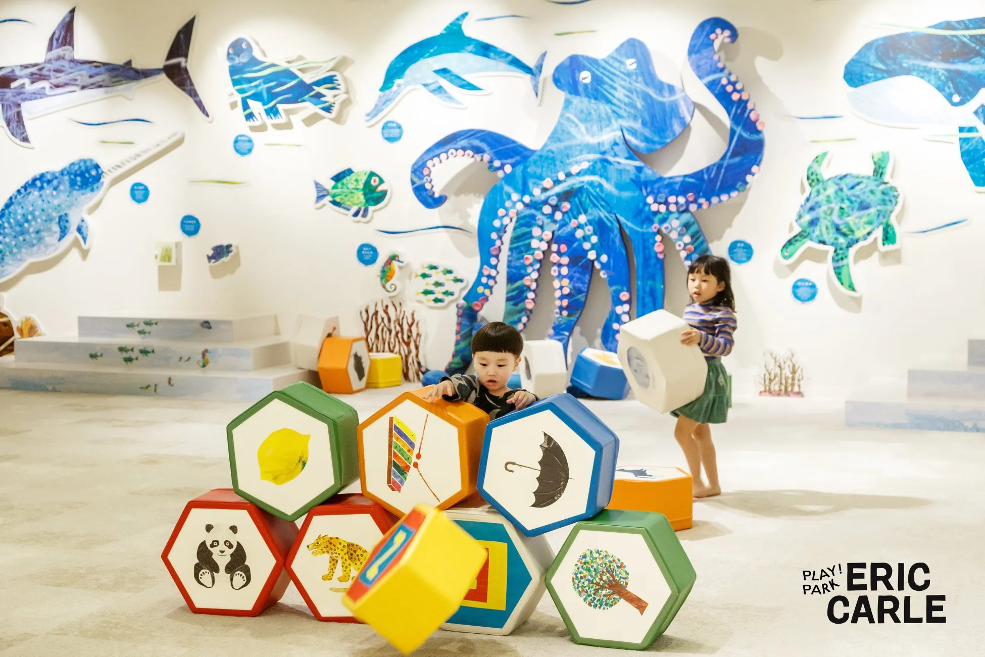 子供たちが遊んでいる様子。壁には海の生き物の絵が飾られ、床には六角形のブロックが置かれています。