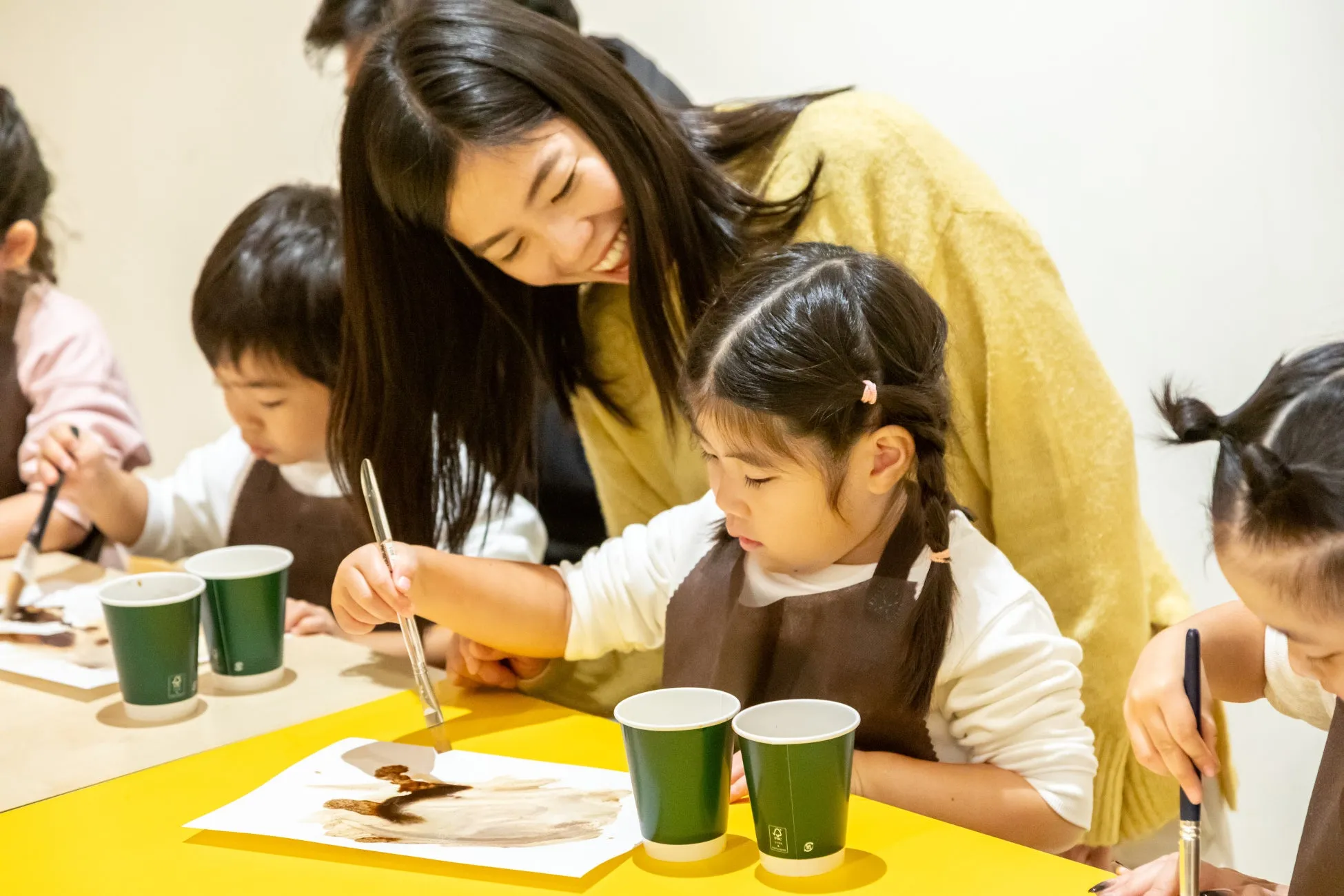 子供たちが絵を描くワークショップの様子。女性が子供たちを見守りながら、楽しそうに絵筆を動かしている。