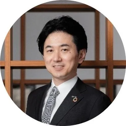 スーツを着た笑顔の日本人男性が丸いフレームの中に写っています。