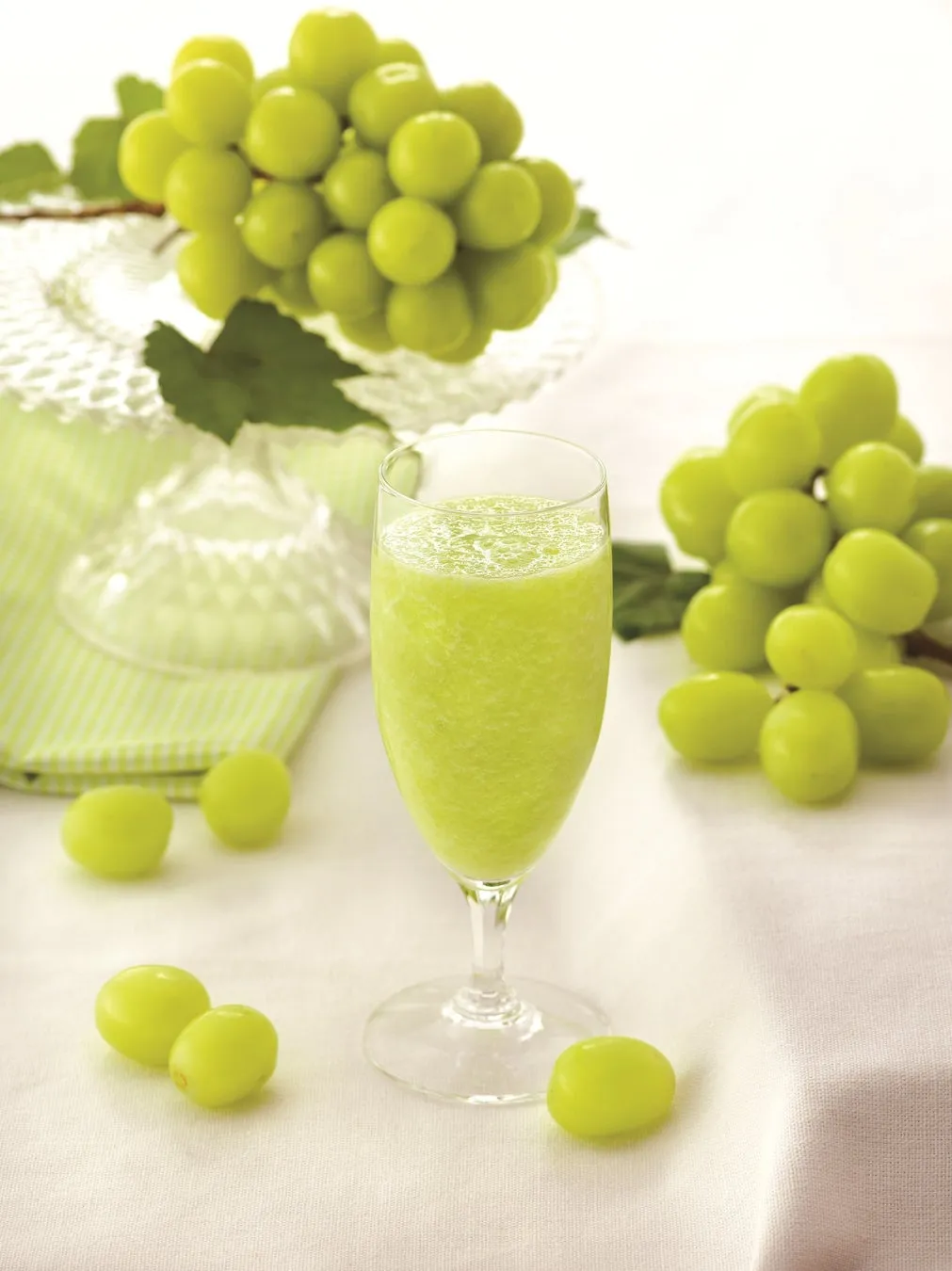 シャインマスカットの爽やかなグリーンスムージーのイメージ写真。グラスに注がれたスムージーと、テーブルに置かれたシャインマスカットの房が、夏の涼しげな雰囲気を醸し出しています。