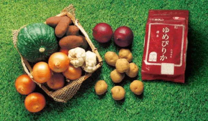 カボチャ、タマネギ、サツマイモ、ジャガイモ、赤カブ、ニンニクなどの野菜と、ゆめぴりかのパッケージが芝生の上に配置された写真です。