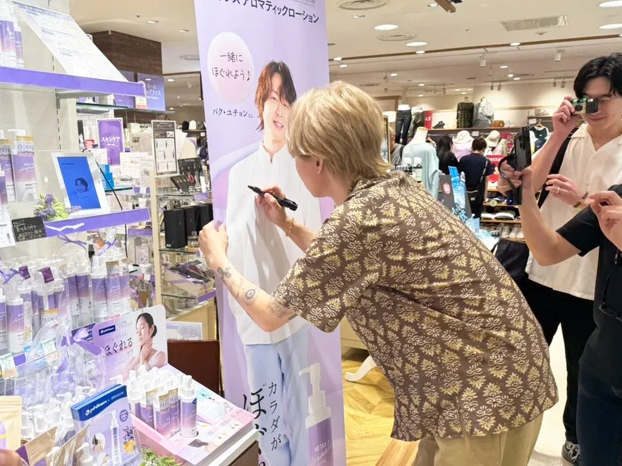 ある男性が、パク・ユチョンのポスターにサインをしている様子を写した写真です。周りには、商品が陳列されている店内の様子が写っています。