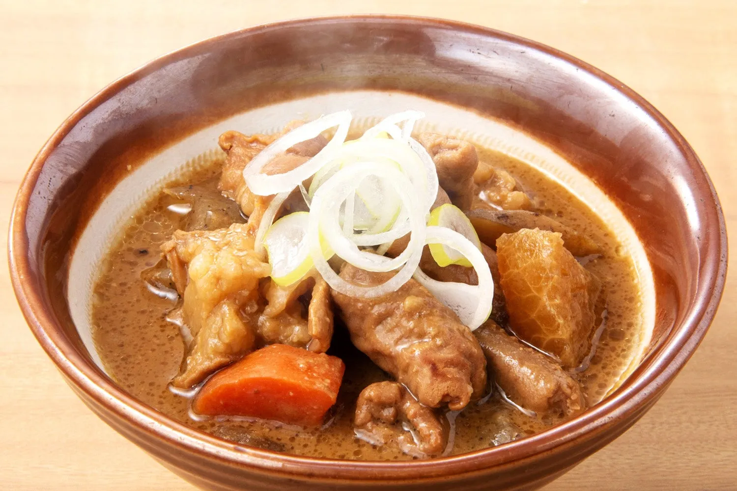 茶色の丼に入った、煮込み料理の写真。具材は、大根、人参、ネギなど。