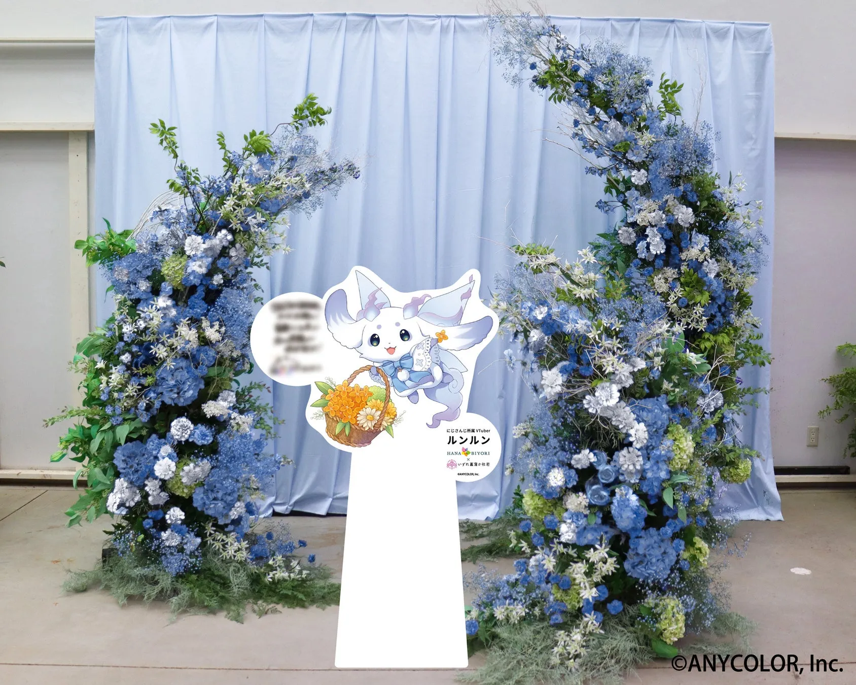 青い花で飾られたアーチと、キャラクターのルンルンのイラストが描かれた看板。