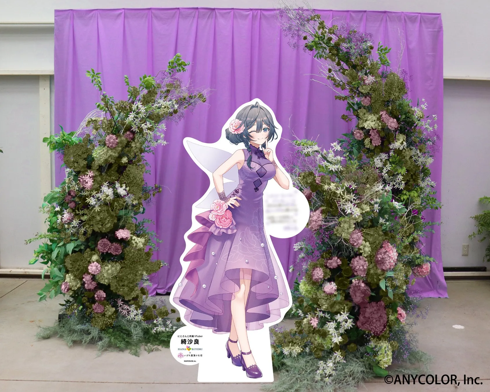 紫色のカーテンを背景に、花で飾られたアーチと、VTuberの綺沙良の等身大パネル。