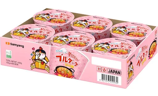 ピンク色の箱に入ったSamyangのブルタックラーメンのパッケージ。箱には複数のカップ麺が入っており、それぞれにブルタックのロゴとキャラクターが描かれている。