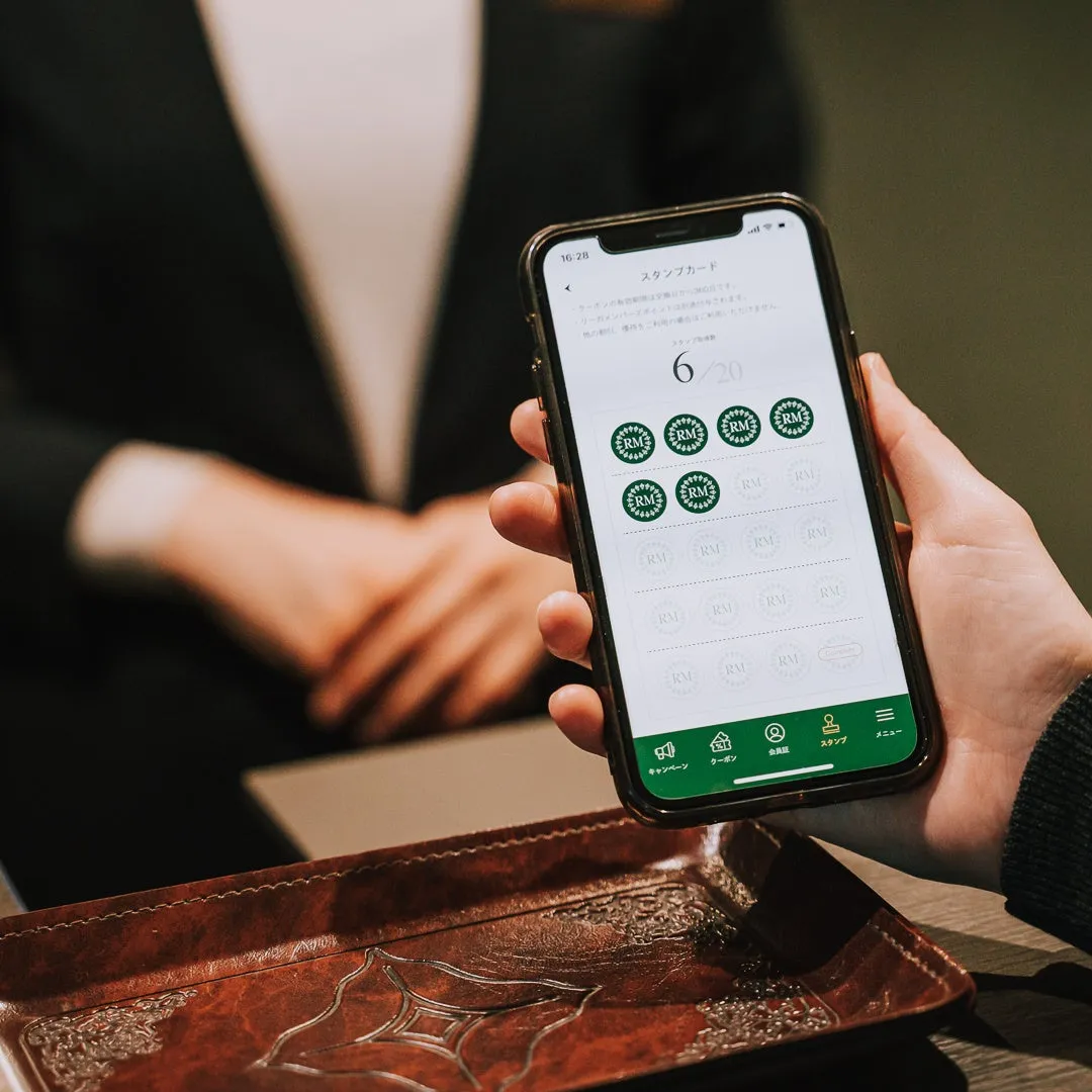 スマートフォンに表示されたスタンプカードの画像。6/20のスタンプが押されており、RMのロゴが見える。手前のトレーが印象的。
