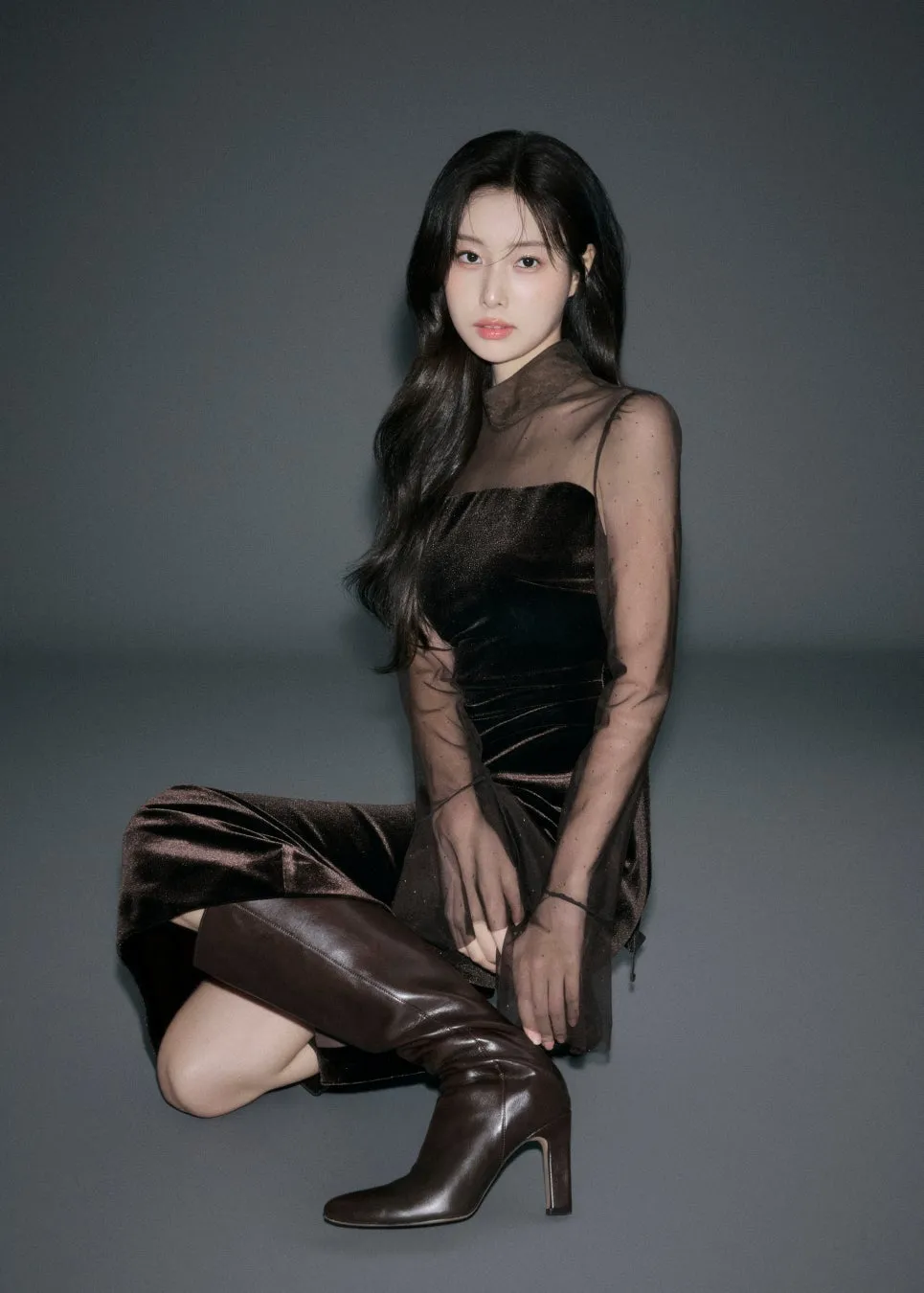 茶色のドレスを着て、膝を抱える女性の写真です。彼女は茶色のブーツを履いており、長い黒髪をしています。